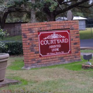 A brick sign for Courtyard Assisted Living surrounded by greenery.