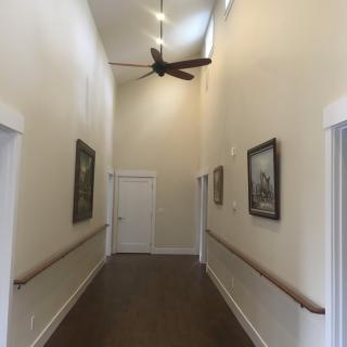 A long hallway with paintings, a ceiling fan, and handrails along the walls.