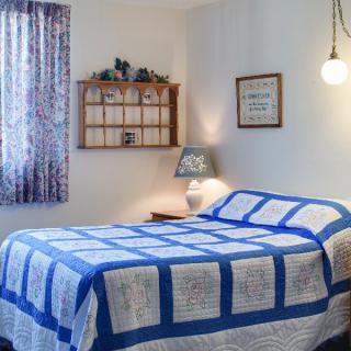A cozy bedroom with a blue and white quilt on the bed, featuring a lamp and decorated walls.