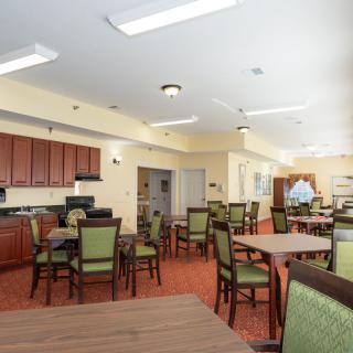 A spacious dining area with multiple tables and chairs, featuring a kitchen area in the background.