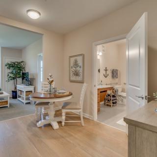 A cozy home interior featuring a dining area with round table and chairs, adjacent to a living room and bathroom.