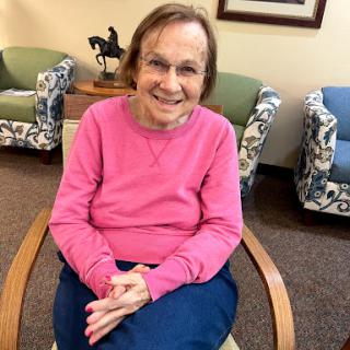 An elderly woman smiles warmly while sitting in a cozy indoor setting.