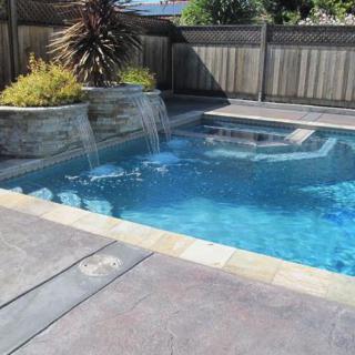 A backyard swimming pool with a small waterfall feature and surrounding patio area.