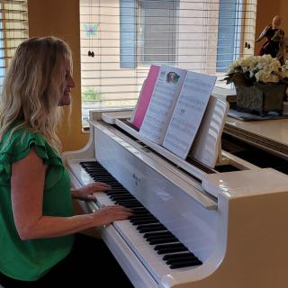 A woman plays the piano while reading sheet music in a well-lit room.
