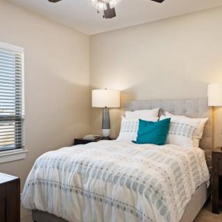 A cozy bedroom featuring a neatly made bed with striped bedding, flanked by two nightstands and lamps, and a window letting in natural light.