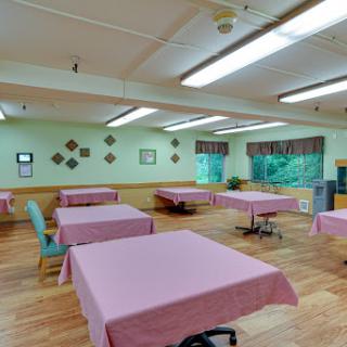 A spacious room with pink tablecloth-covered tables and a warm wooden floor, featuring green walls and ample lighting.