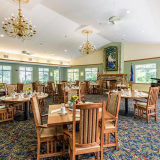 A spacious and elegantly decorated dining room with wooden tables and chairs, featuring chandeliers and large windows.