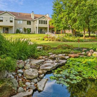 A beautiful house surrounded by a lush garden with a pond and trees.