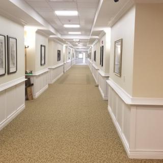 A long hallway with carpeted flooring and framed pictures on the walls.