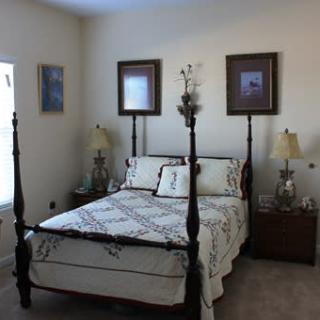 A cozy bedroom featuring a four-poster bed with elegant bedding, flanked by bedside tables and lamps, adorned with framed artwork on the walls.