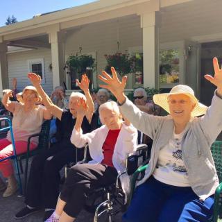 A group of seniors sitting outside, waving and smiling in a cheerful atmosphere.