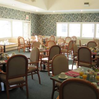 An empty dining room with neatly arranged tables and chairs, featuring large windows and decorative wallpaper.