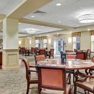 A spacious dining area with multiple tables and chairs, featuring elegant ceiling lights and a carpeted floor.