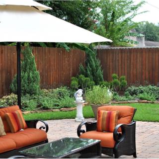 A cozy backyard patio with outdoor seating and a large umbrella, surrounded by well-maintained garden landscaping.