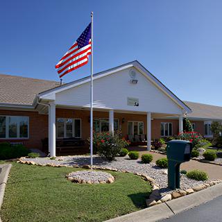 A building with an American flag flying in front, surrounded by well-maintained landscaping.