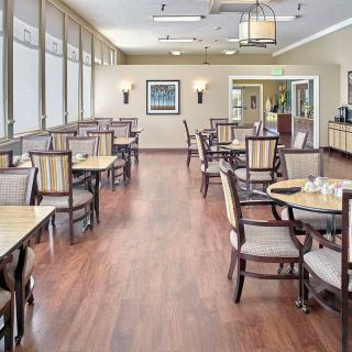 A bright and spacious dining area with neatly arranged tables and chairs, featuring wood flooring and large windows.