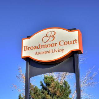 A sign for Broadmoor Court Assisted Living against a clear blue sky.