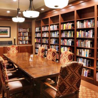 A cozy library conference room with wooden bookshelves and a large table surrounded by chairs.
