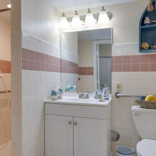 A small bathroom featuring a vanity with a mirror, overhead lighting, and tiled walls.