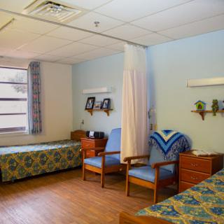 A spacious hospital patient room featuring two beds and a comfortable seating area.
