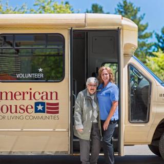 An elderly person and an assistant standing next to a community service bus.