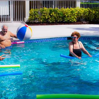 Seniors enjoying a sunny day in the pool with noodles and a beach ball.