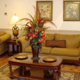 A cozy living room with a floral centerpiece on a wooden coffee table, surrounded by sofas and artwork on the walls.
