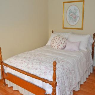 A cozy bedroom featuring a bed with a wooden frame, adorned with a quilt and pillows, and an artwork hanging on the wall.
