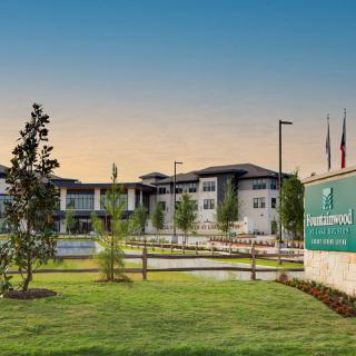 A modern building complex with well-maintained lawns and a prominent sign at sunset.