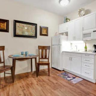 A cozy kitchen and dining area featuring white cabinets, a small table with two chairs, and decorative artwork on the walls.
