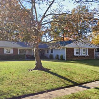 A suburban ranch-style house with a well-maintained lawn and a tree in the front yard during autumn.