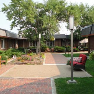 A peaceful courtyard with lush greenery, benches, and a brick pathway.