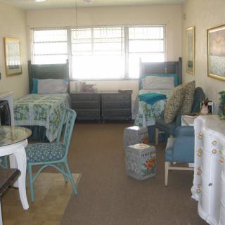 A cozy living room with twin beds, wicker chairs, and ample natural light.