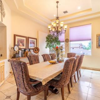 A spacious dining room with a long table, surrounded by elegant chairs and illuminated by a chandelier.