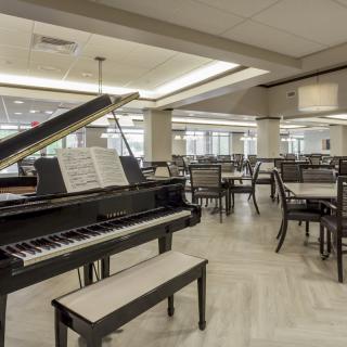 A grand piano in a spacious dining area with tables and chairs.