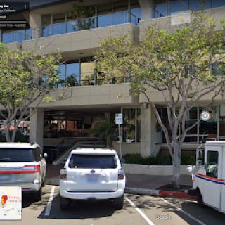A view of a multi-story building with parking spaces filled with vehicles and trees lining the sides.