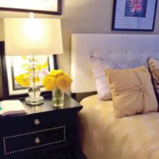 A cozy bedroom with a lamp, nightstand, and decorative flowers.