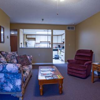 A cozy living room with a sofa, armchair, and coffee table, adjacent to an open kitchen area.