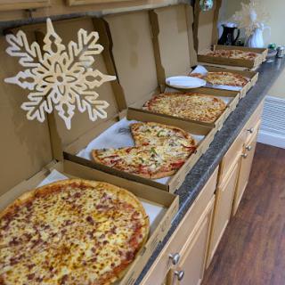 An array of pizzas displayed in their boxes, topped with various ingredients, set up in a cozy kitchen.