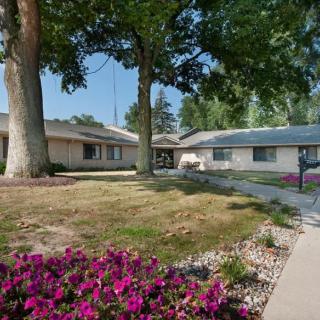 A suburban bungalow with a landscaped front yard, featuring trees and vibrant flowers.