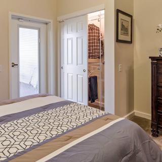 A cozy bedroom with a neatly made bed, an open closet, and a dresser.