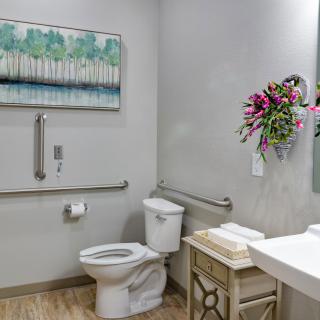 A well-decorated bathroom with a toilet, sink, and mirror, featuring floral decor and wall art.
