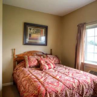 A cozy bedroom with a wooden bed frame, colorful bedding, and a large window letting in natural light.