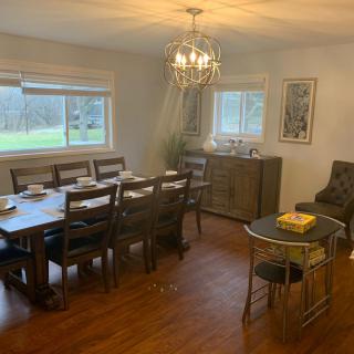 A cozy dining room with a large table, multiple chairs, and a chandelier, featuring natural light from the windows.