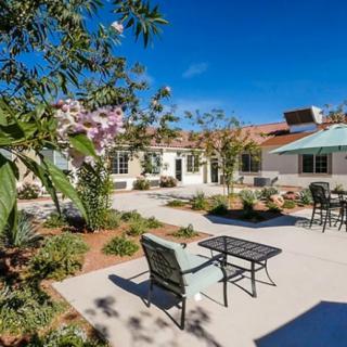 A serene outdoor patio area with chairs and tables surrounded by lush landscaping on a sunny day.