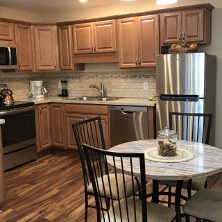 A modern kitchen with wooden cabinets and stainless steel appliances, featuring a round dining table with chairs.
