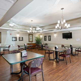 A spacious dining area with multiple tables and chairs, featuring elegant chandeliers and wood flooring.