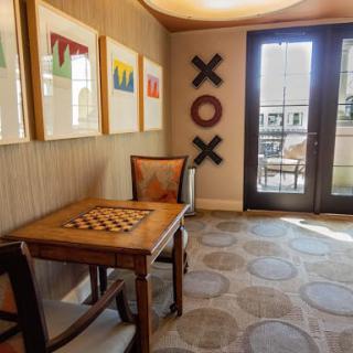 A cozy room with a chessboard table, decorated with colorful artwork and sunlight streaming through the doors.
