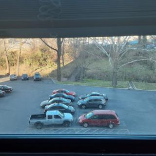 A view of a parking lot with several cars parked and trees in the background.