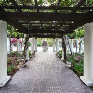 A serene garden pathway framed by columns and a trellis, inviting visitors to explore.